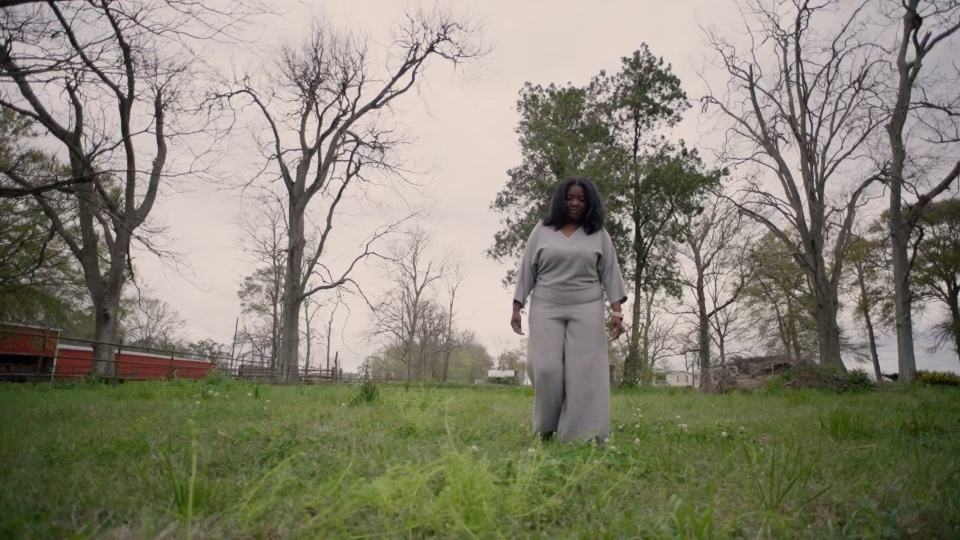 A woman standing alone in a field of bare trees: still from Infertile Ground